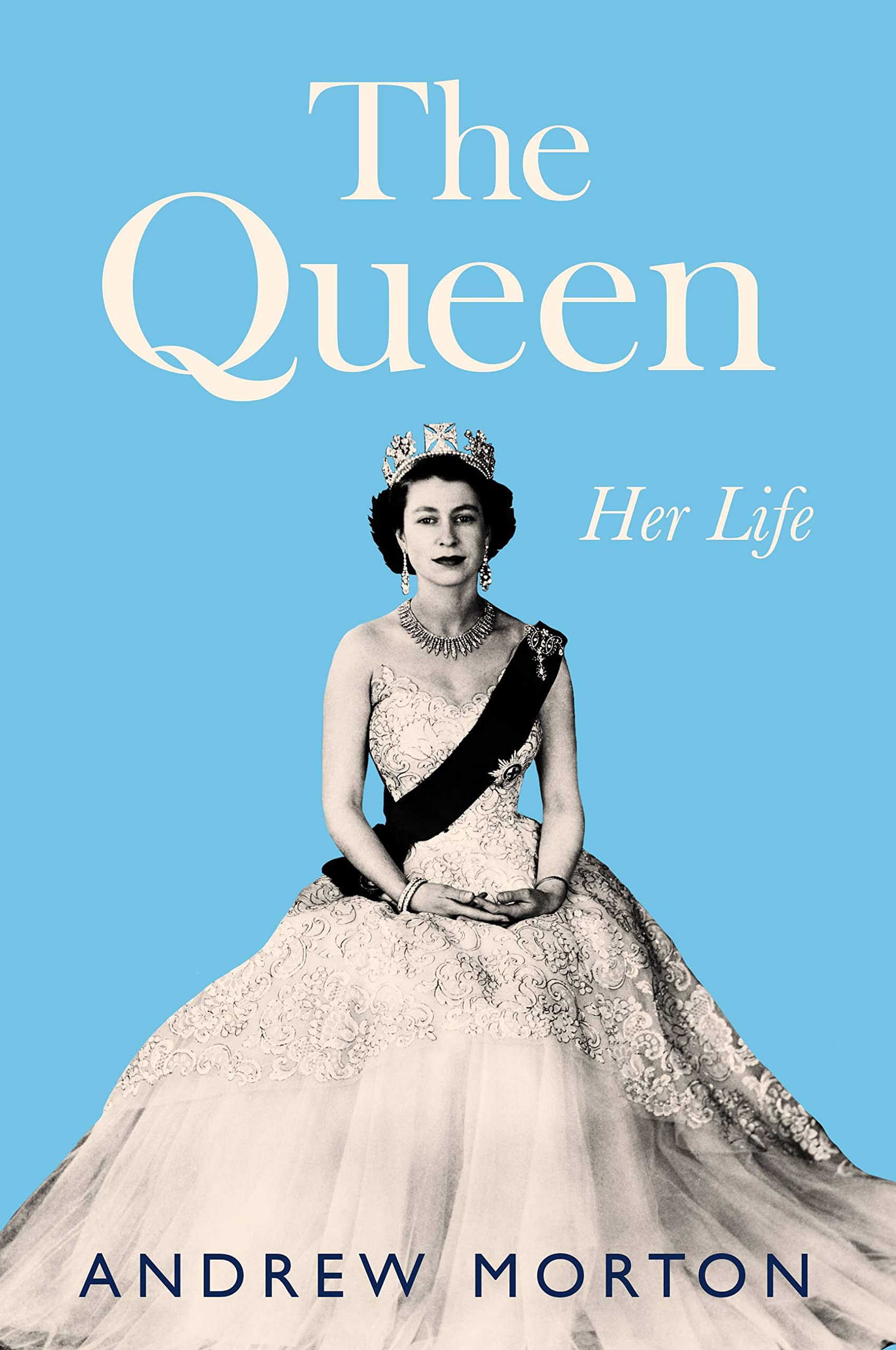 Solid Blue Background. Black and white photo of Queen Elizabeth II in floral dress with sash and tierra. The Queen Her Life by Andrew Morton.