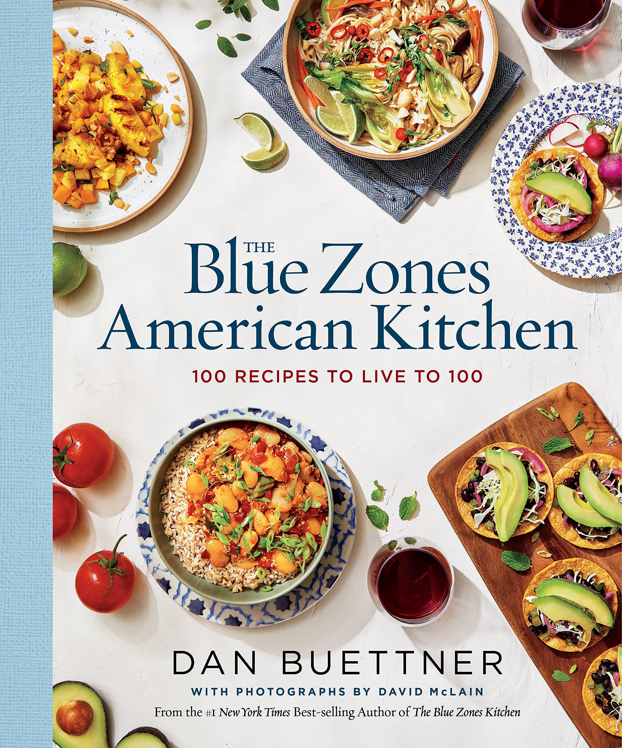 Light blue book spine on left hand side of book. Background features 5 different dishes if American food dishes. The Blue Zone American Kitchen: 100 recipes to live to 100 by Dan Buettner.